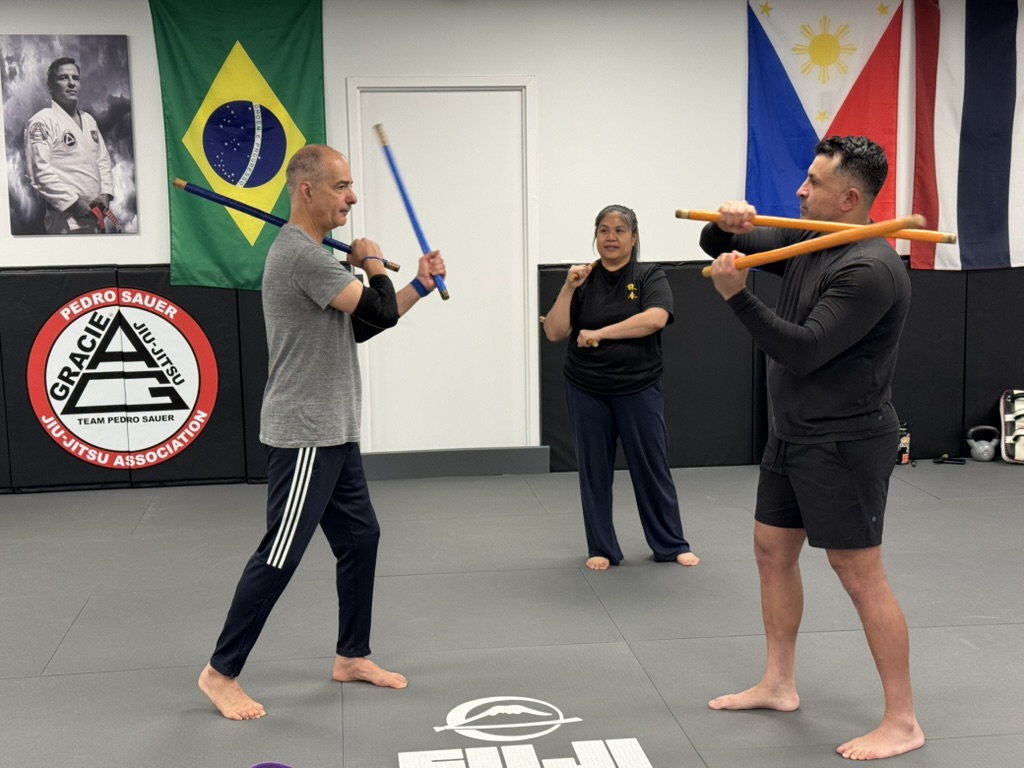 Kali students practicing coordinated stick drills while an instructor observes at Pedro Sauer Academy