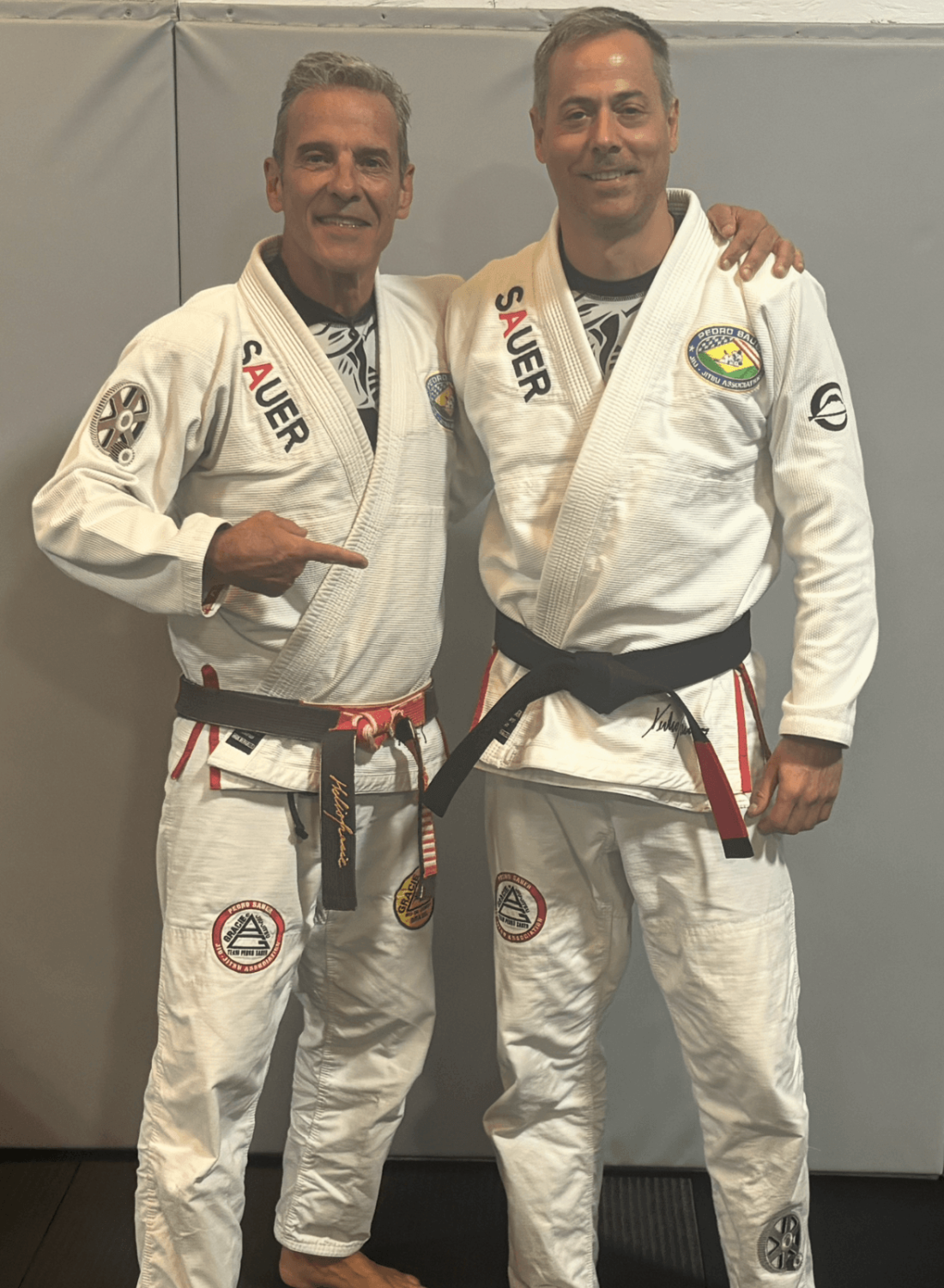Coach Tom Luke standing with Professor Pedro Sauer after earning his Brazilian Jiu-Jitsu black belt at a Pedro Sauer Association black belt gathering in Georgia during 2026.
