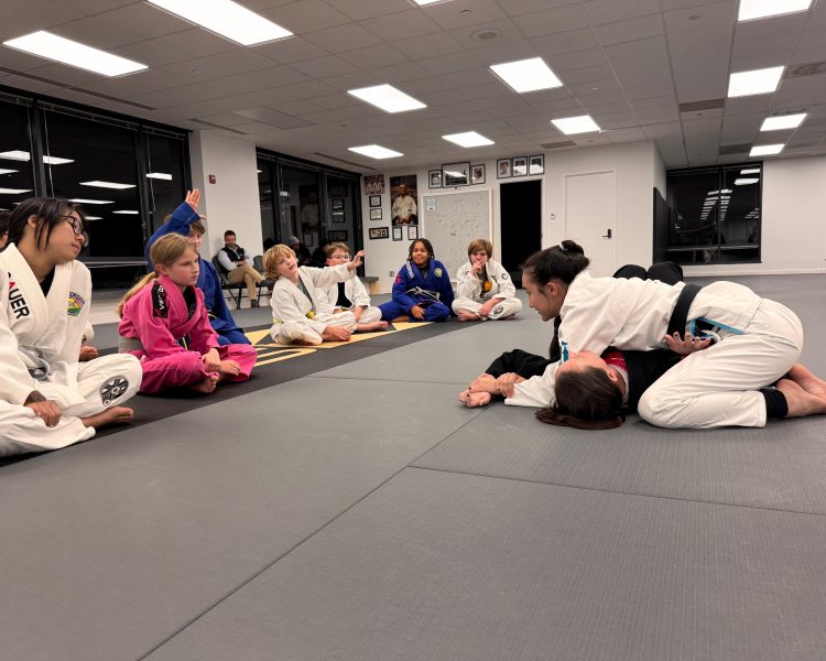 Coach Nina demonstrating an Americana submission on Coach Dana during a youth Brazilian Jiu-Jitsu gi class at Pedro Sauer Academy of Self-Defense in Herndon, VA.