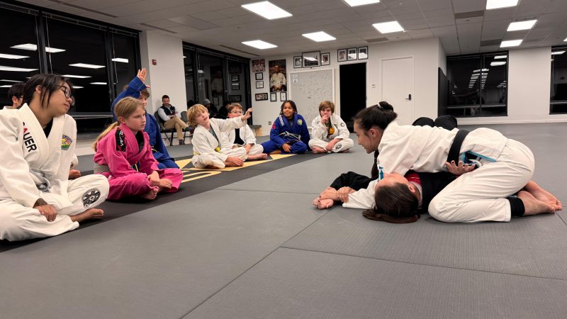 Coach Nina demonstrating an Americana submission on Coach Dana during a youth Brazilian Jiu-Jitsu gi class at Pedro Sauer Academy of Self-Defense in Herndon, VA.