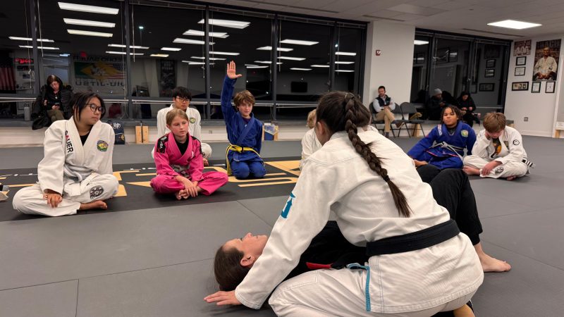 Youth Brazilian Jiu-Jitsu gi class at Pedro Sauer Academy of Self-Defense in Herndon, VA, with Coach Nina demonstrating a side-control escape.